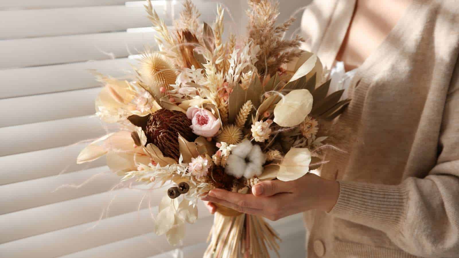 A close up view of a woman holding a beautiful dried flower bouquet near the window